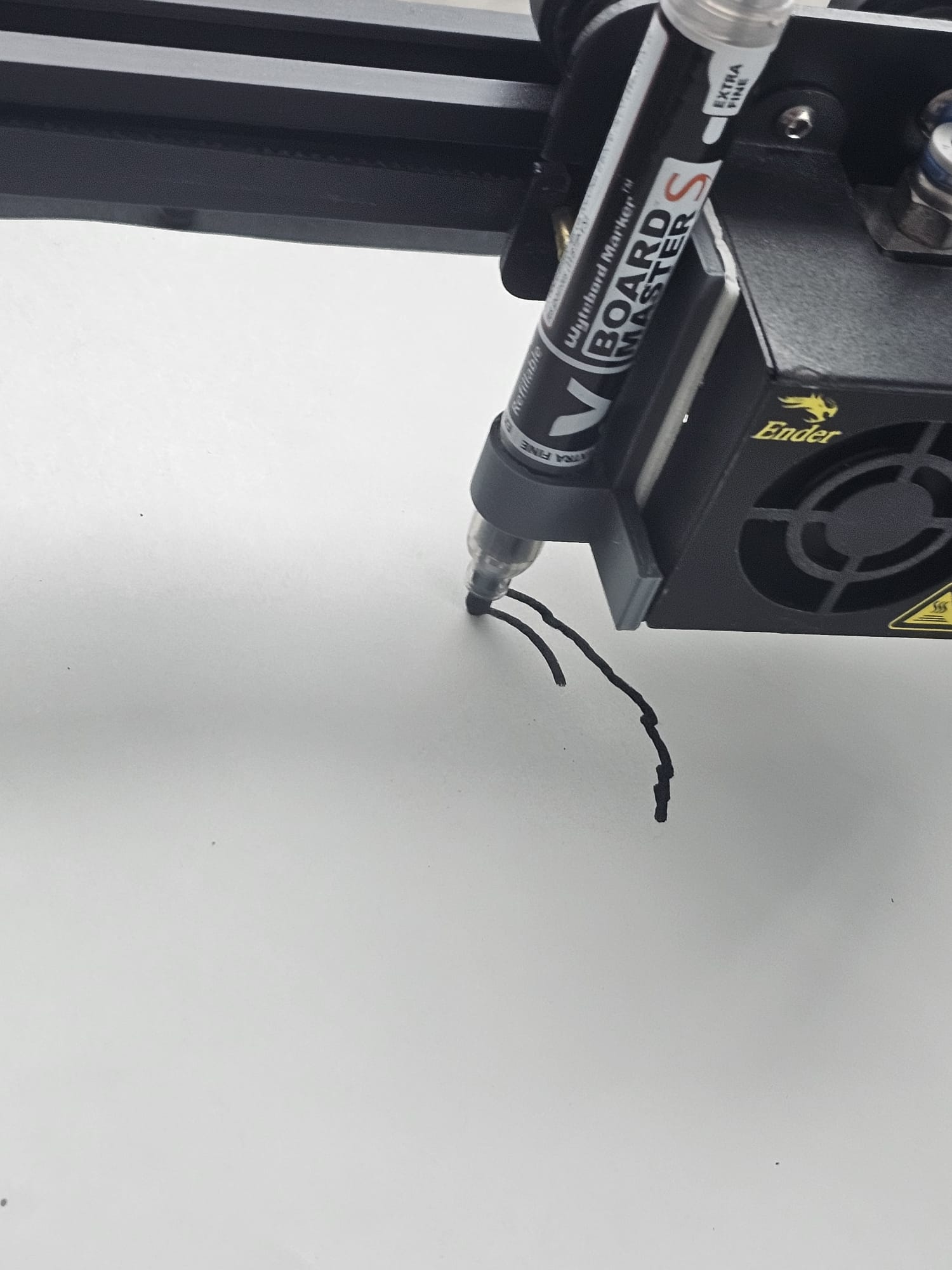 Close-up of the print head: a Board Master whiteboard marker clamped to the carriage right next to the hot end, its tip touching the paper.