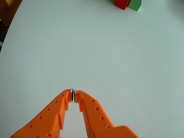 Close-up from the other gripper camera: same orange gripper and white table, but red and green cubes are visible in the corner of the frame.